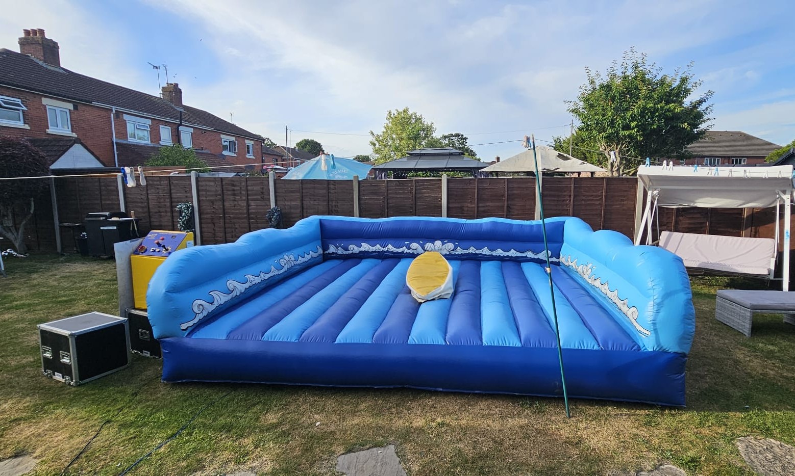 Inflatable surf simulator set up on a lawn with control unit and equipment cases